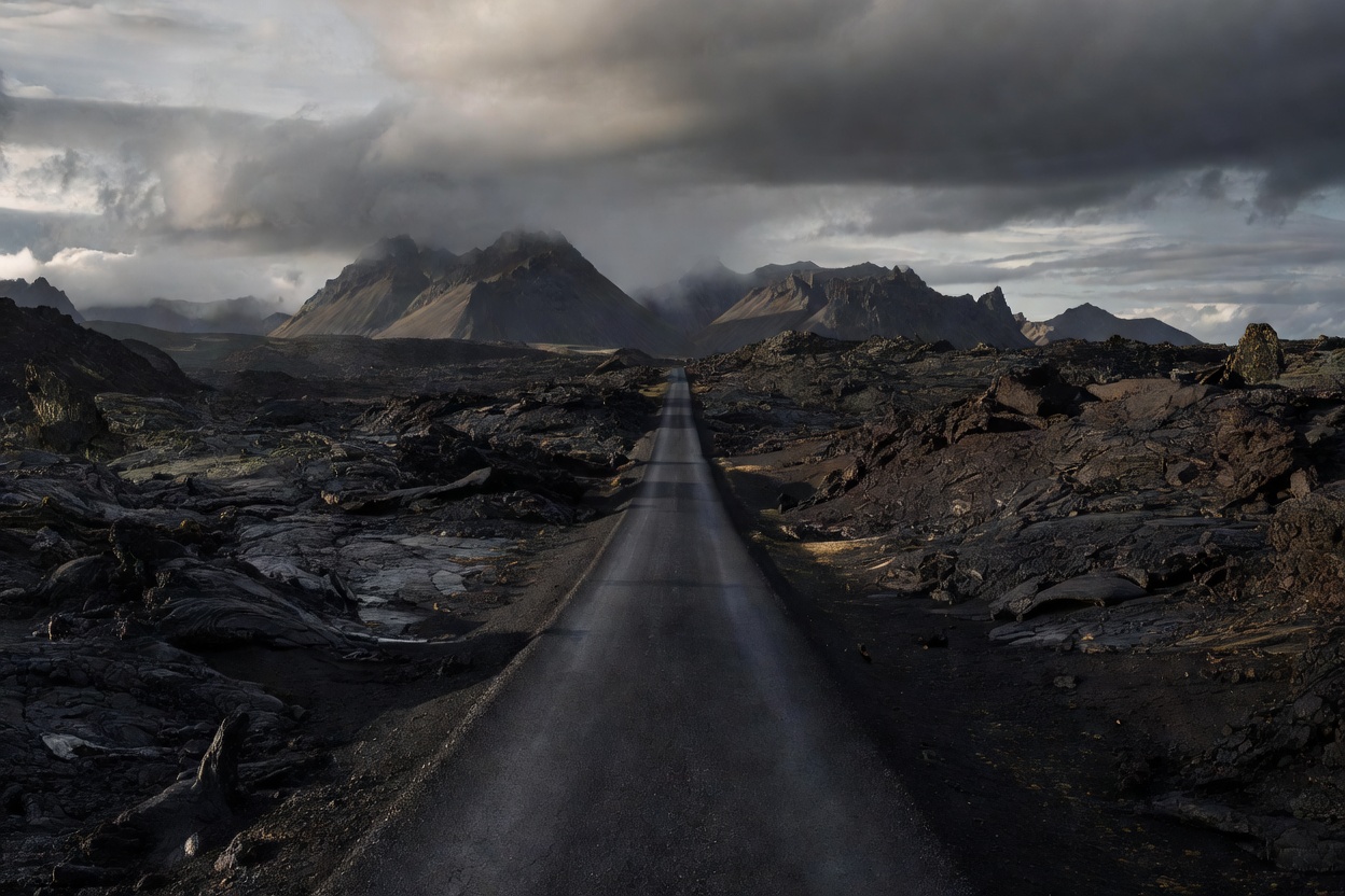 Asphalt road cutting through dramatic black lava fields towards distant mountains in Iceland